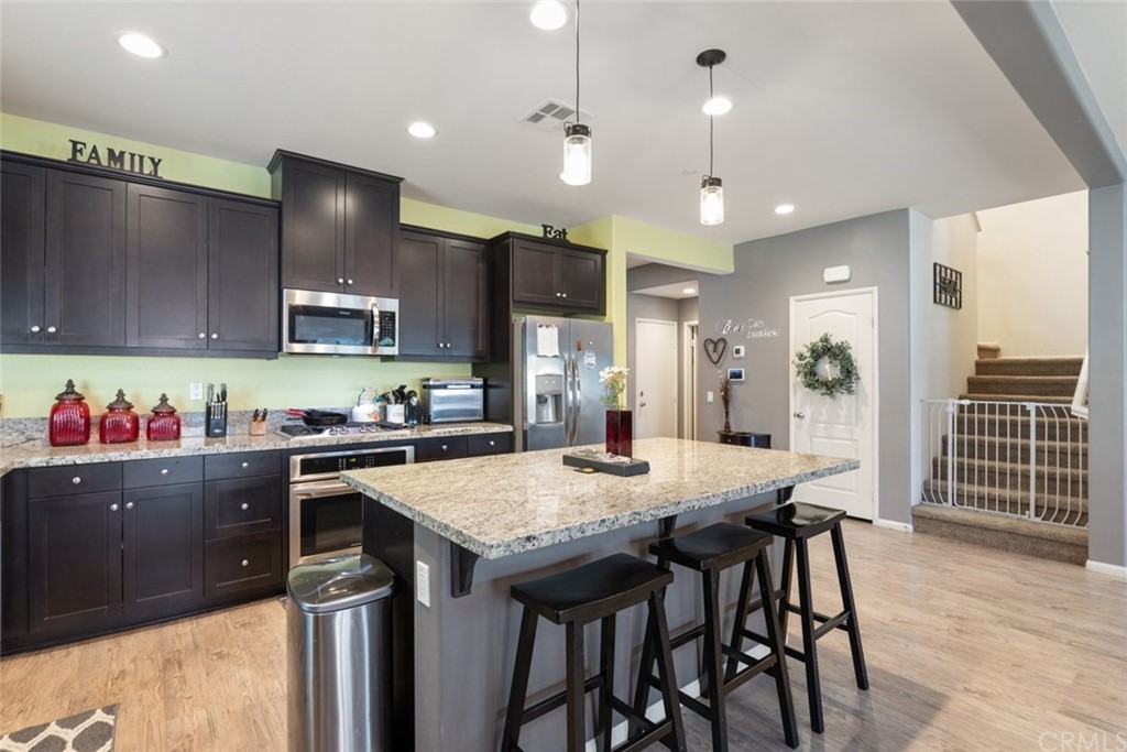 24802 Sandy Trail Place Menifee, CA 92584 - Photo 17 of 42 a kitchen with granite countertop a table chairs stainless steel appliances and wooden floor