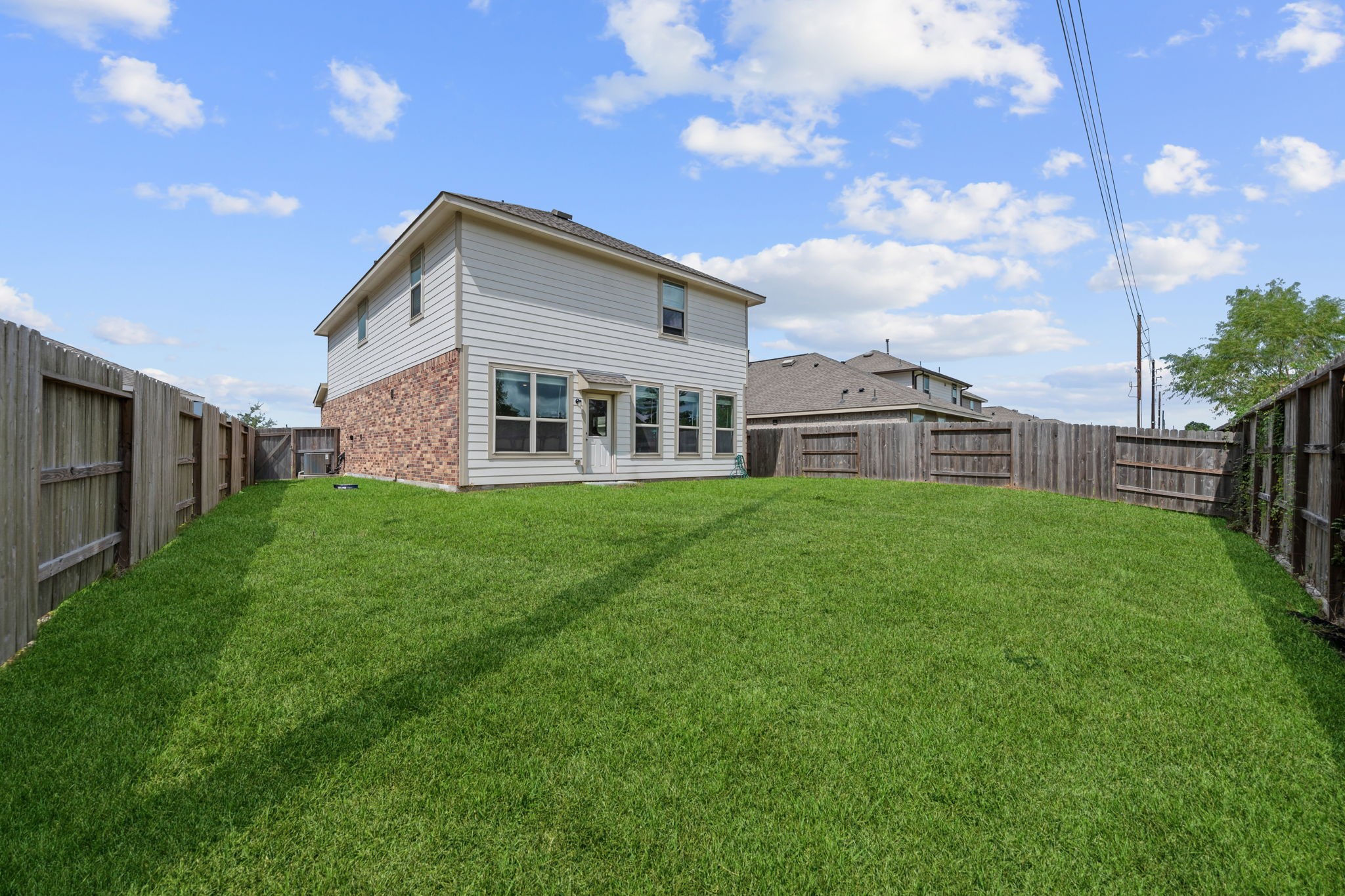 3043 Marble Rise Trail Porter, TX 77365 - Photo 26 of 27 Spacious backyard with lush green grass, perfect for outdoor activities, enclosed by a wooden fence for privacy, complementing a charming two-story home.