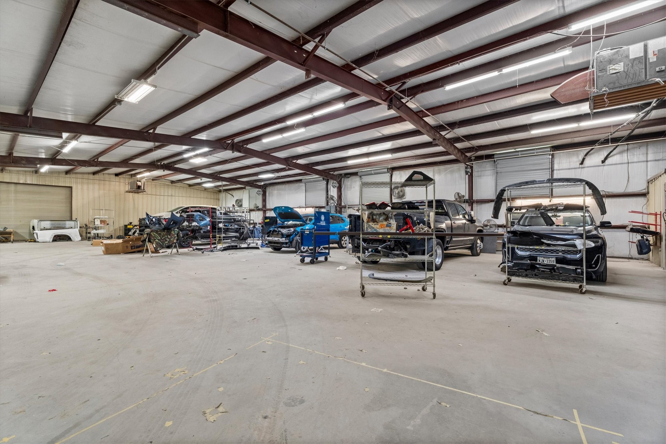 11066 Sh 242 Conroe, TX 77385 - Photo 21 of 21 This photo shows a spacious industrial garage with a high metal ceiling, ample lighting, and several vehicles and equipment inside, ideal for automotive work or storage needs.