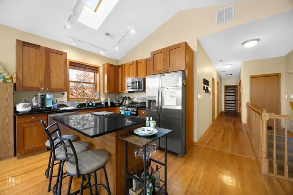 a kitchen with stainless steel appliances granite countertop a refrigerator a stove a sink dishwasher and a dining table with wooden cabinet