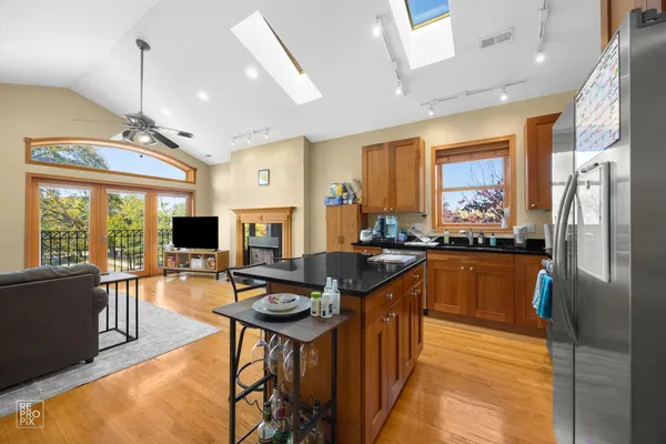 a kitchen with stainless steel appliances kitchen island granite countertop a refrigerator a sink dishwasher a dining table and chairs with wooden floor
