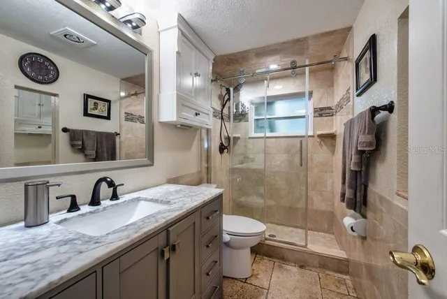 a bathroom with a granite countertop sink a toilet a mirror and shower
