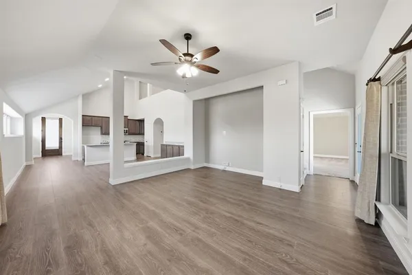 a view of an empty room with wooden floor and a ceiling fan