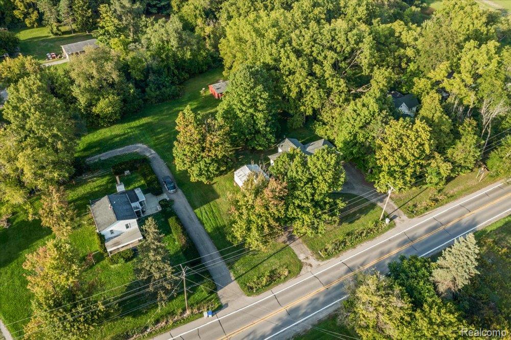 59380 10 Mile Road South Lyon, MI 48178 - Photo 4 of 53 Aerial perspective showcasing a property surrounded by mature trees, featuring a paved driveway, a white-sided residence with a dark roof, and extensive green landscaping
