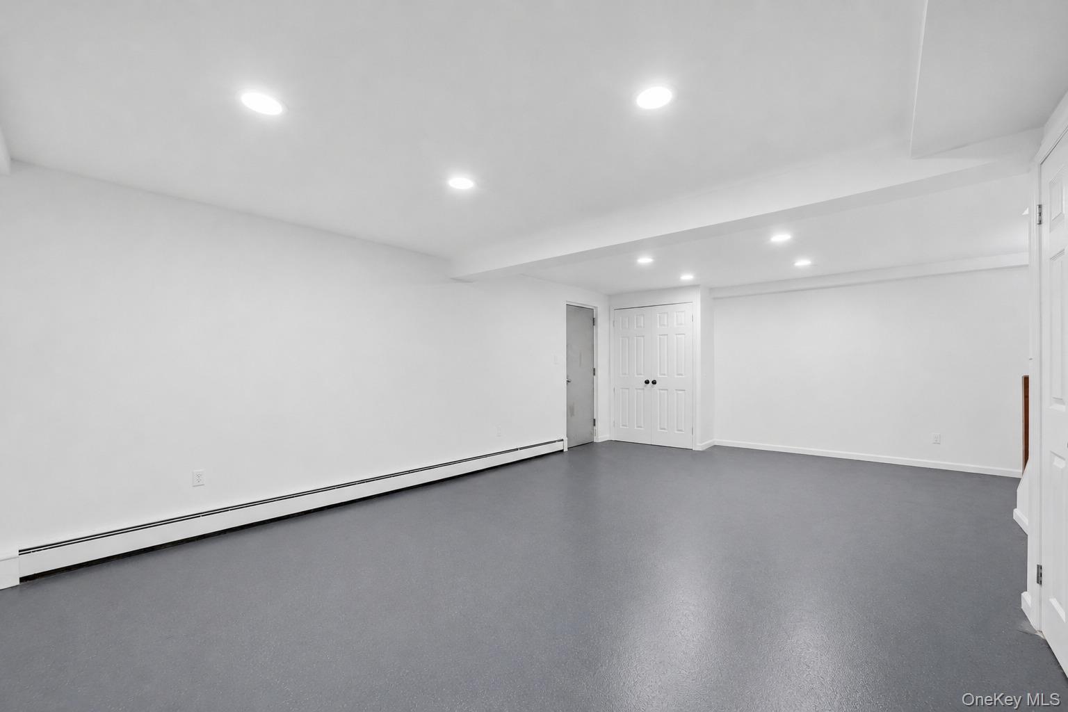 144 Bell Road Scarsdale, NY 10583 - Photo 34 of 49 Spacious basement recreation room featuring gray flooring, recessed lighting, multiple paneled closet doors with black hardware, and a staircase with a wood handrail