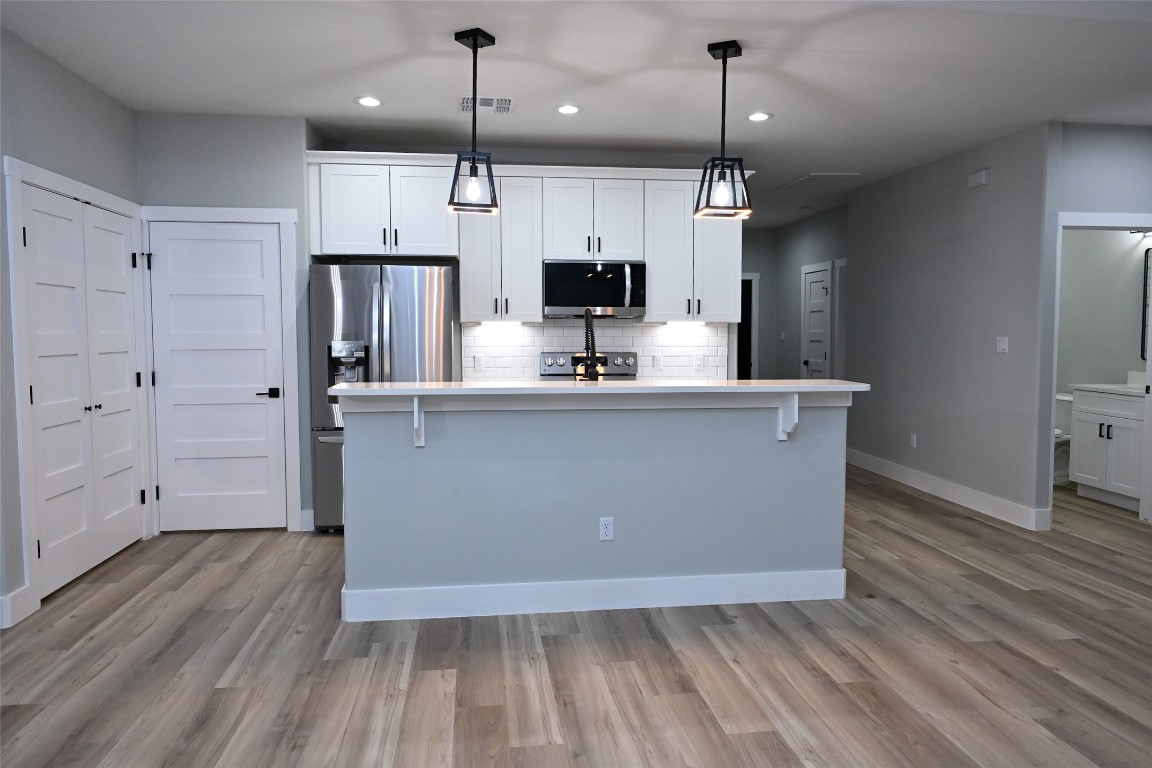 516 North Hackberry Avenue Luling, TX 78648 - Photo 13 of 36 Kitchen with white cabinetry, a kitchen island with sink, stainless steel appliances, hanging light fixtures, and decorative backsplash