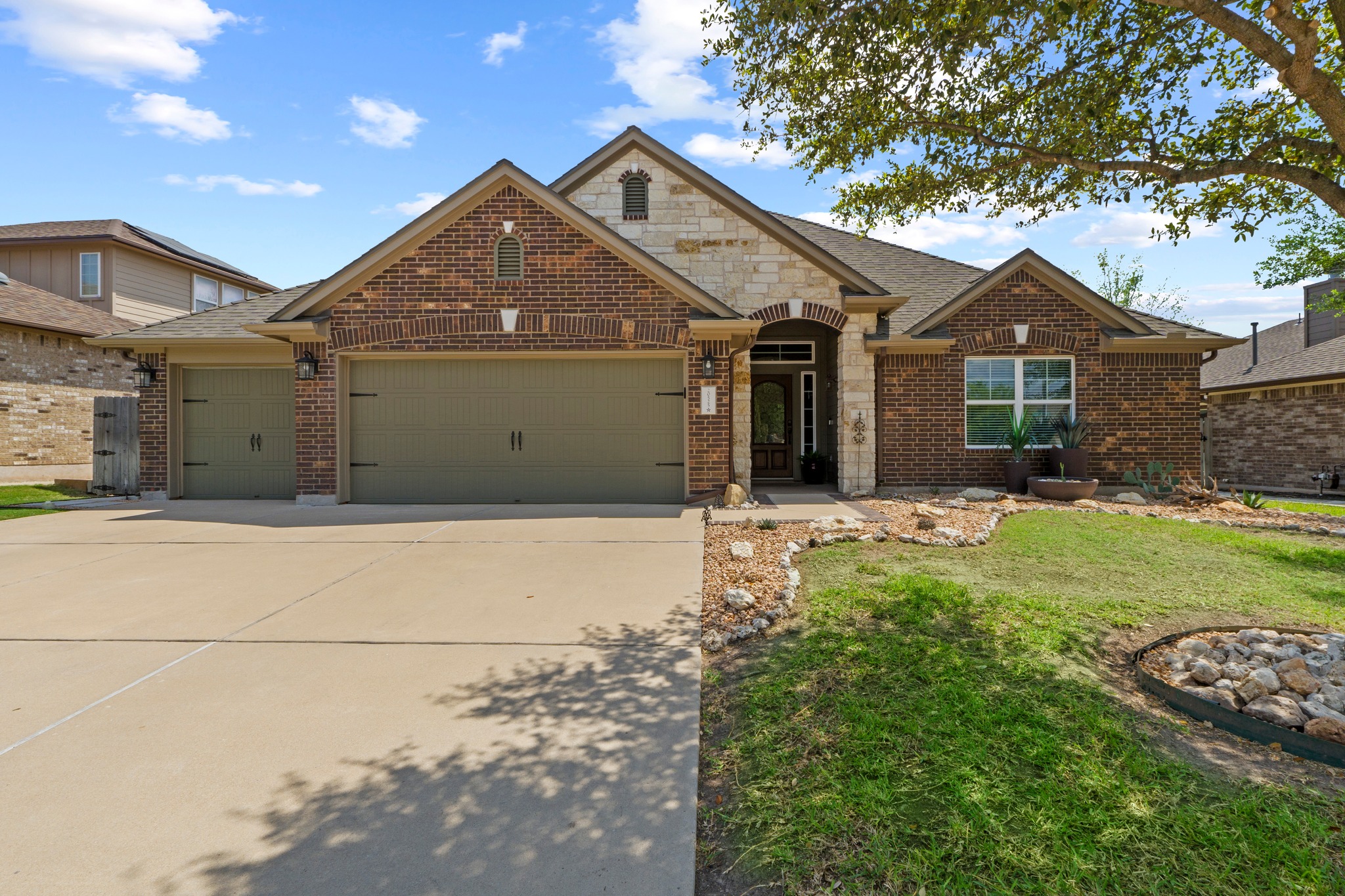 View of front of property featuring an attached 3-car extended garage, brick siding, concrete driveway, a front lawn, and stone siding
