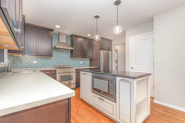 a kitchen with stainless steel appliances granite countertop a sink a stove a refrigerator and island with wooden floor