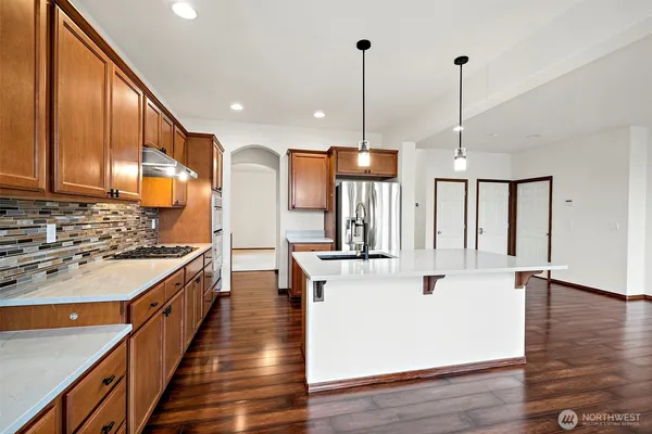 a kitchen with stainless steel appliances kitchen island granite countertop a stove a refrigerator a sink and a wooden floor