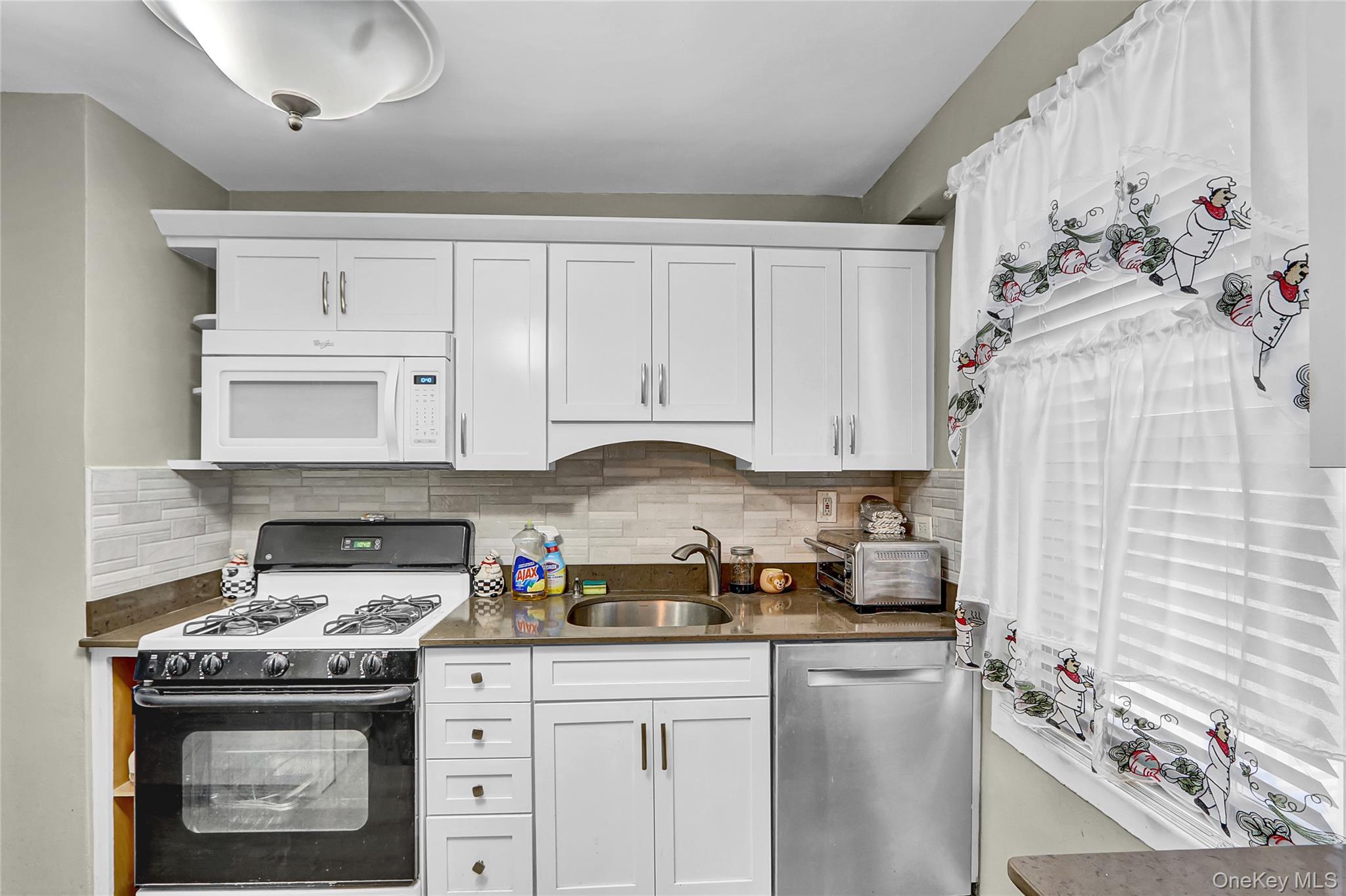 123-40 83rd Avenue, Unit 6D Queens, NY 11415 - Photo 5 of 14 Kitchen featuring range with gas cooktop, white microwave, dishwasher, white cabinetry, and tasteful backsplash