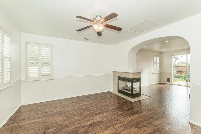 an empty room with wooden floor ceiling fan and windows