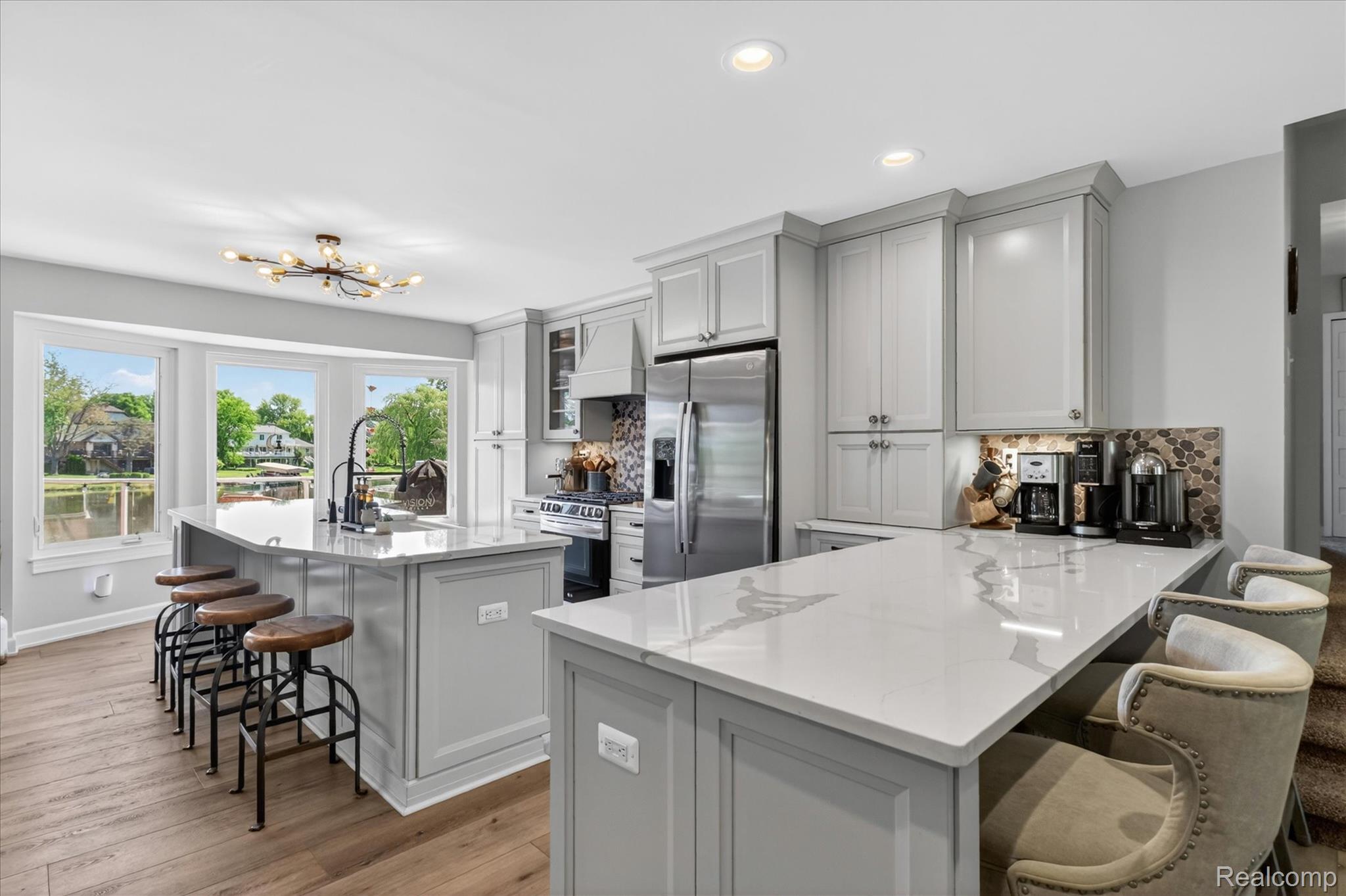 3860 East Commerce Road Commerce Township, MI 48382 - Photo 15 of 72 Modern kitchen featuring two islands with white countertops, light gray cabinetry, stainless steel appliances, and wood-finish flooring