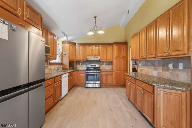 a kitchen with stainless steel appliances granite countertop a refrigerator a sink dishwasher a stove and white cabinets with wooden floor