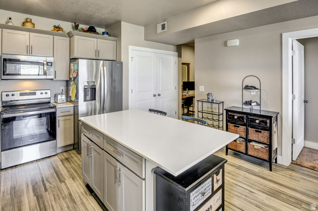 2101 North Main Street, Unit 306 Sunset, UT 84015 - Photo 5 of 22 Modern kitchen featuring a large central island with a light-toned countertop, stainless steel appliances, neutral cabinetry, and wood-finish flooring