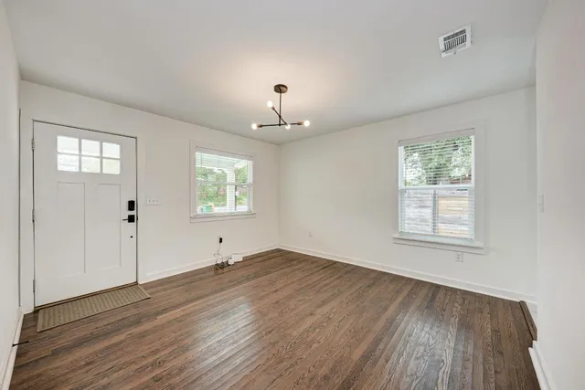 an empty room with wooden floor chandelier and windows