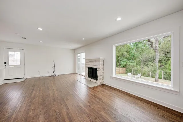 an empty room with wooden floor fireplace and windows