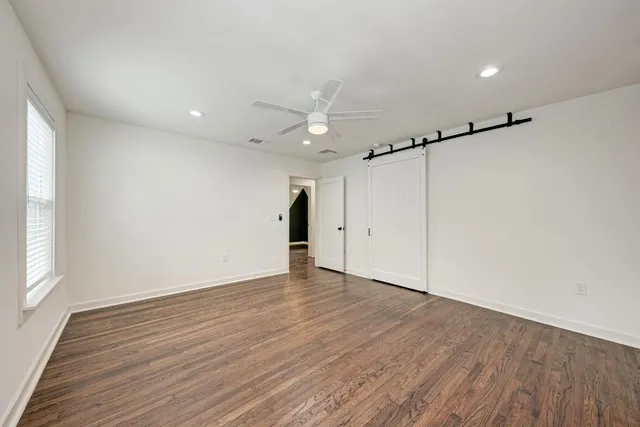 an empty room with wooden floor ceiling fan and windows