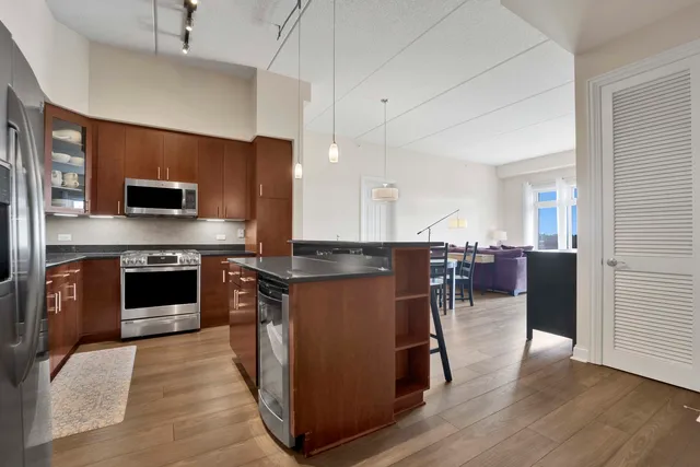 a kitchen with stainless steel appliances granite countertop a stove top oven a sink dishwasher a refrigerator and a dining table with wooden floor