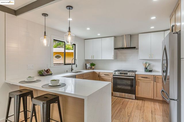 a kitchen with stainless steel appliances granite countertop a sink a stove a refrigerator and island with wooden floor