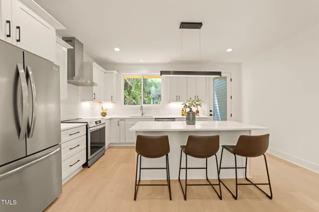 a kitchen with stainless steel appliances a sink a stove a refrigerator and white cabinets with wooden floor