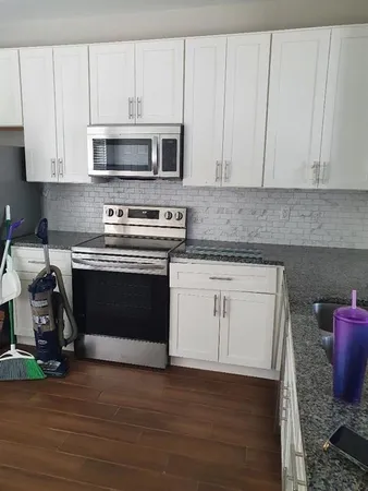 a kitchen with granite countertop white cabinets stainless steel appliances and wooden floor