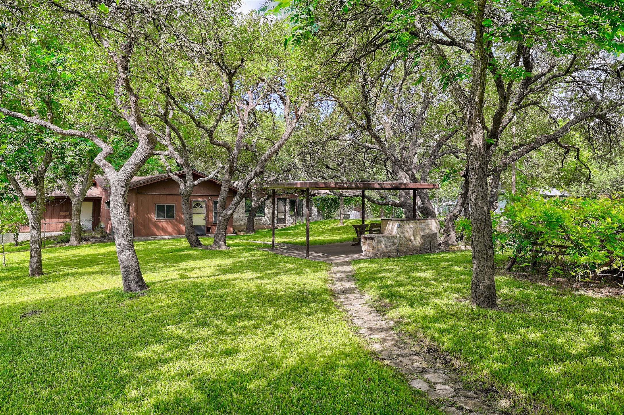 8606 Thunderbird Road, Unit A & B Austin, TX 78736 - Photo 33 of 34 A stone pathway leads to a shaded outdoor living area, nestled amongst mature trees and lush green grass.
