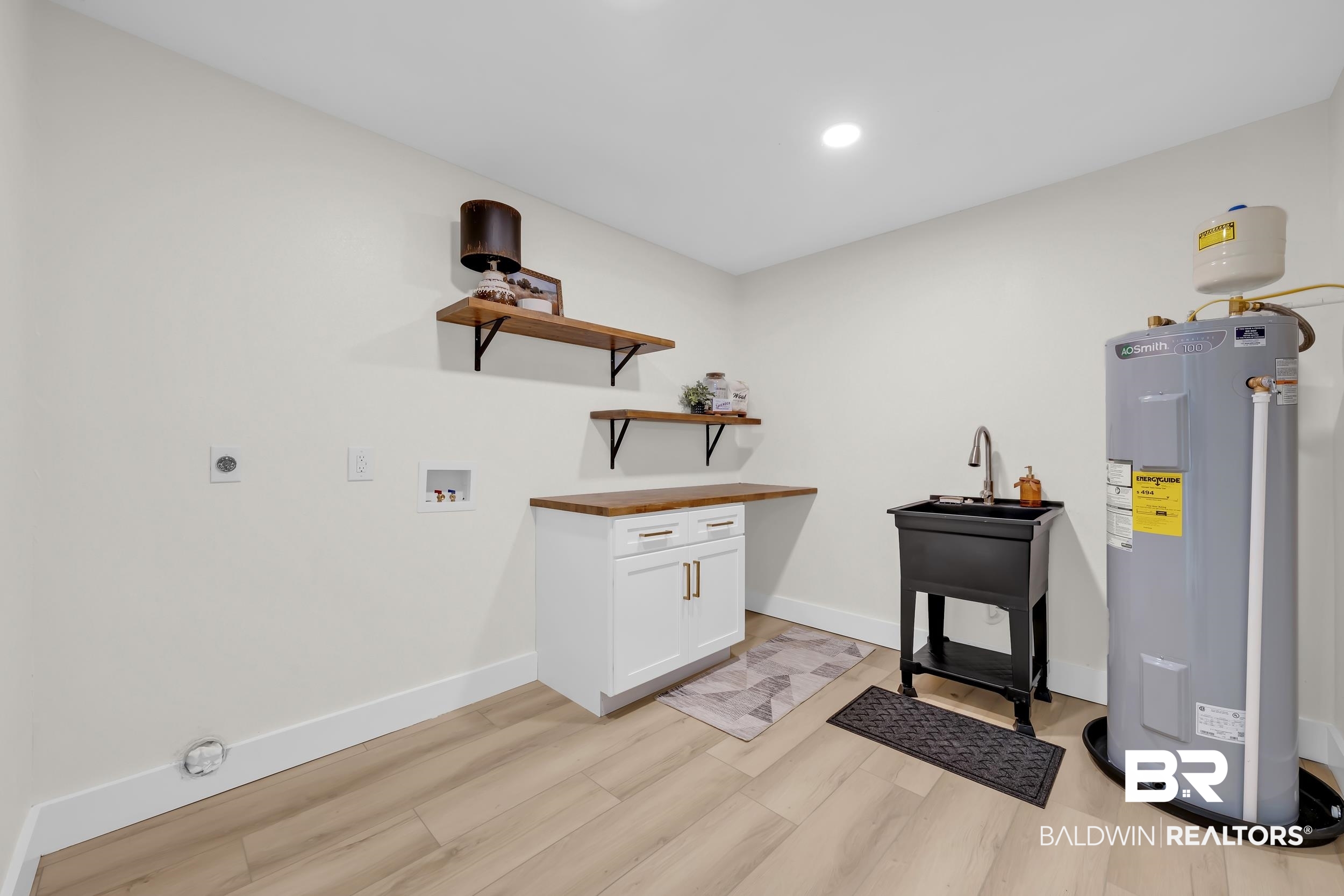 8170 Wilmer Georgetown Road Wilmer, AL 36587 - Photo 23 of 31 Utility room featuring wood-finish flooring, white cabinetry with gold-tone hardware, a built-in utility sink with a high-arch faucet, and open wood shelving