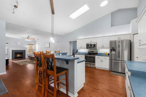 a kitchen with stainless steel appliances kitchen island granite countertop a refrigerator a stove top oven a sink dishwasher and white cabinets with wooden floor