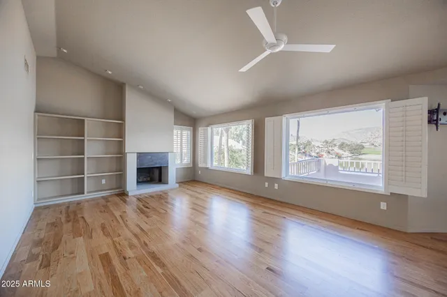 an empty room with wooden floor fireplace and windows