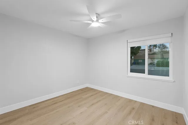 a view of an empty room with wooden floor and a ceiling fan