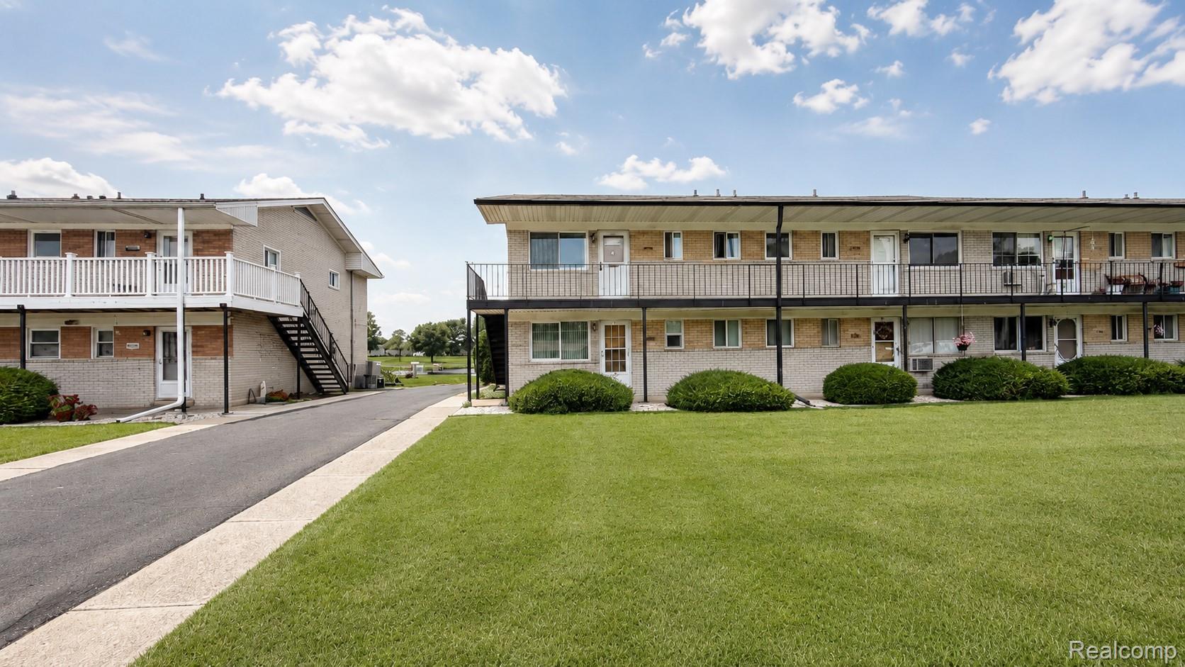 26945 Milford Road, Unit 34 New Hudson, MI 48165 - Photo 2 of 16 Two-story residential buildings featuring brick and siding exteriors, individual balconies with railings, and ground-level patios