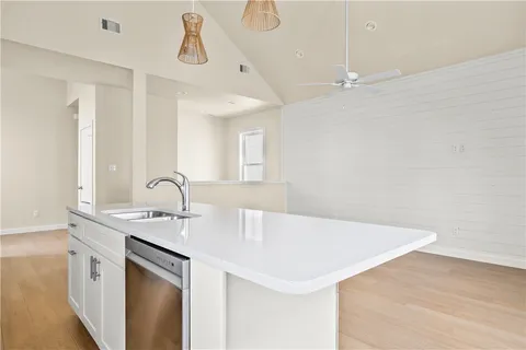 a kitchen with a sink dishwasher and white cabinets with wooden floor