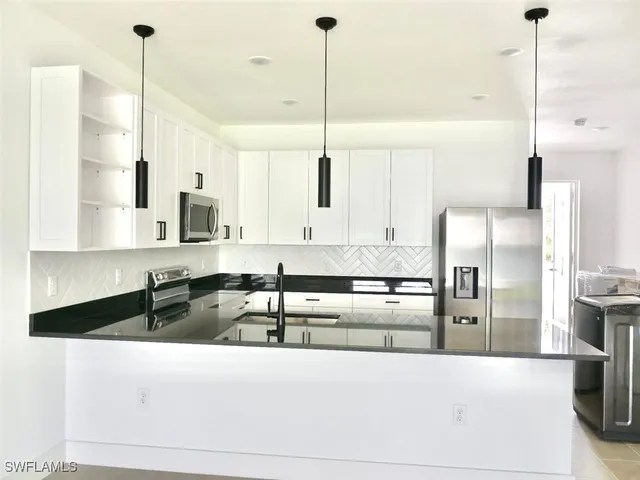 a kitchen with stainless steel appliances kitchen island granite countertop a sink a refrigerator and white cabinets