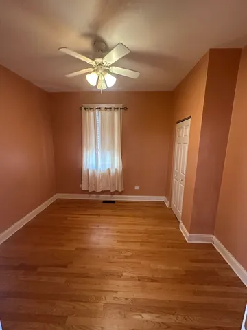 a view of an empty room with wooden floor and fan