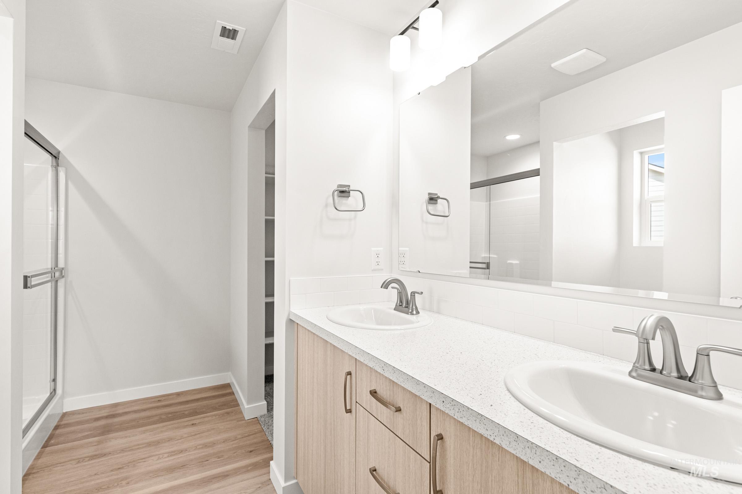 13736 Inman Court Caldwell, ID 83607 - Photo 16 of 20 Full bathroom featuring double vanity, a shower stall, light wood-style floors, and a spacious closet