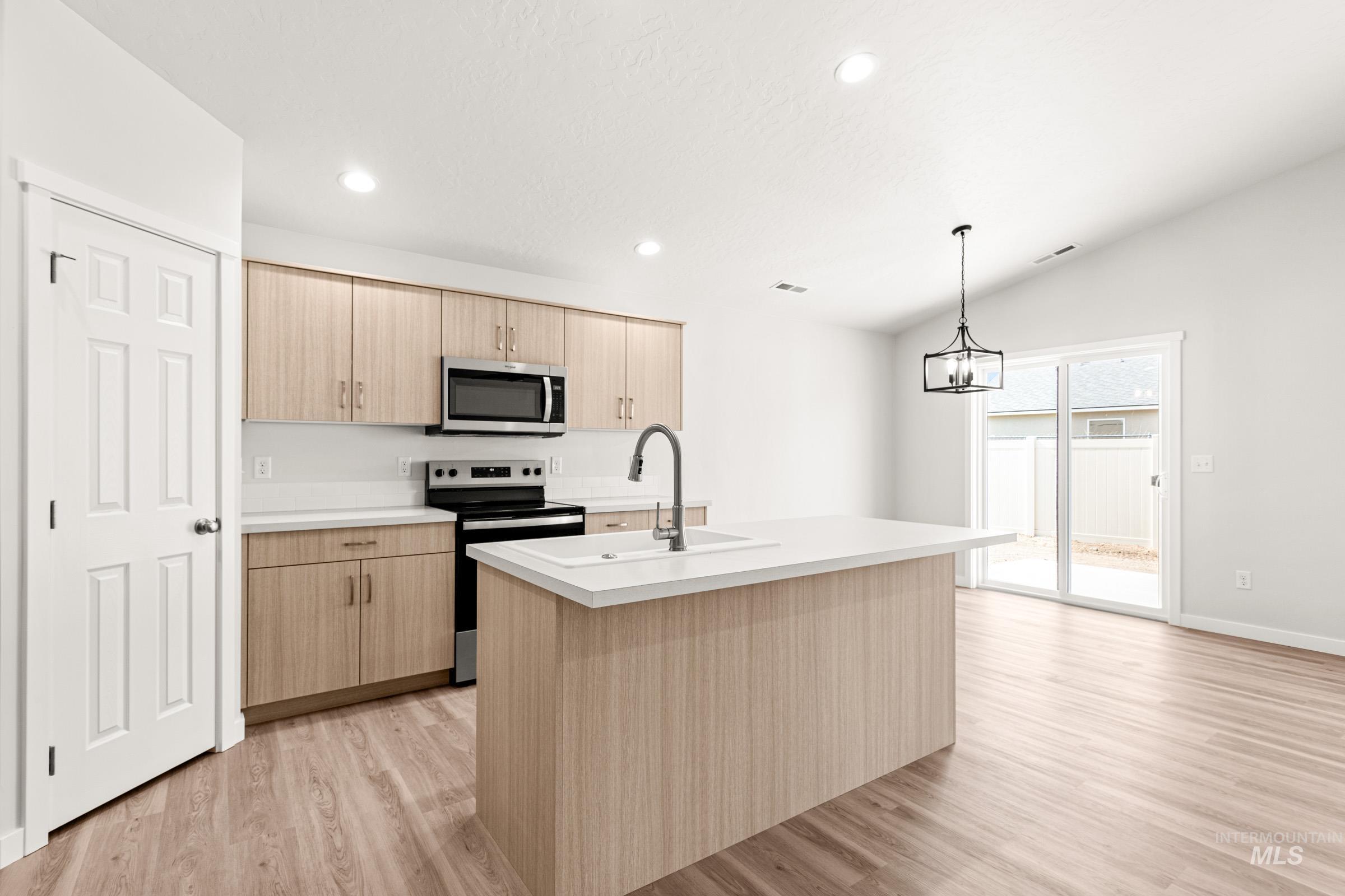 13736 Inman Court Caldwell, ID 83607 - Photo 4 of 20 Kitchen with stainless steel appliances, a kitchen island with sink, light wood finish cabinets, light countertops, and light wood-style floors