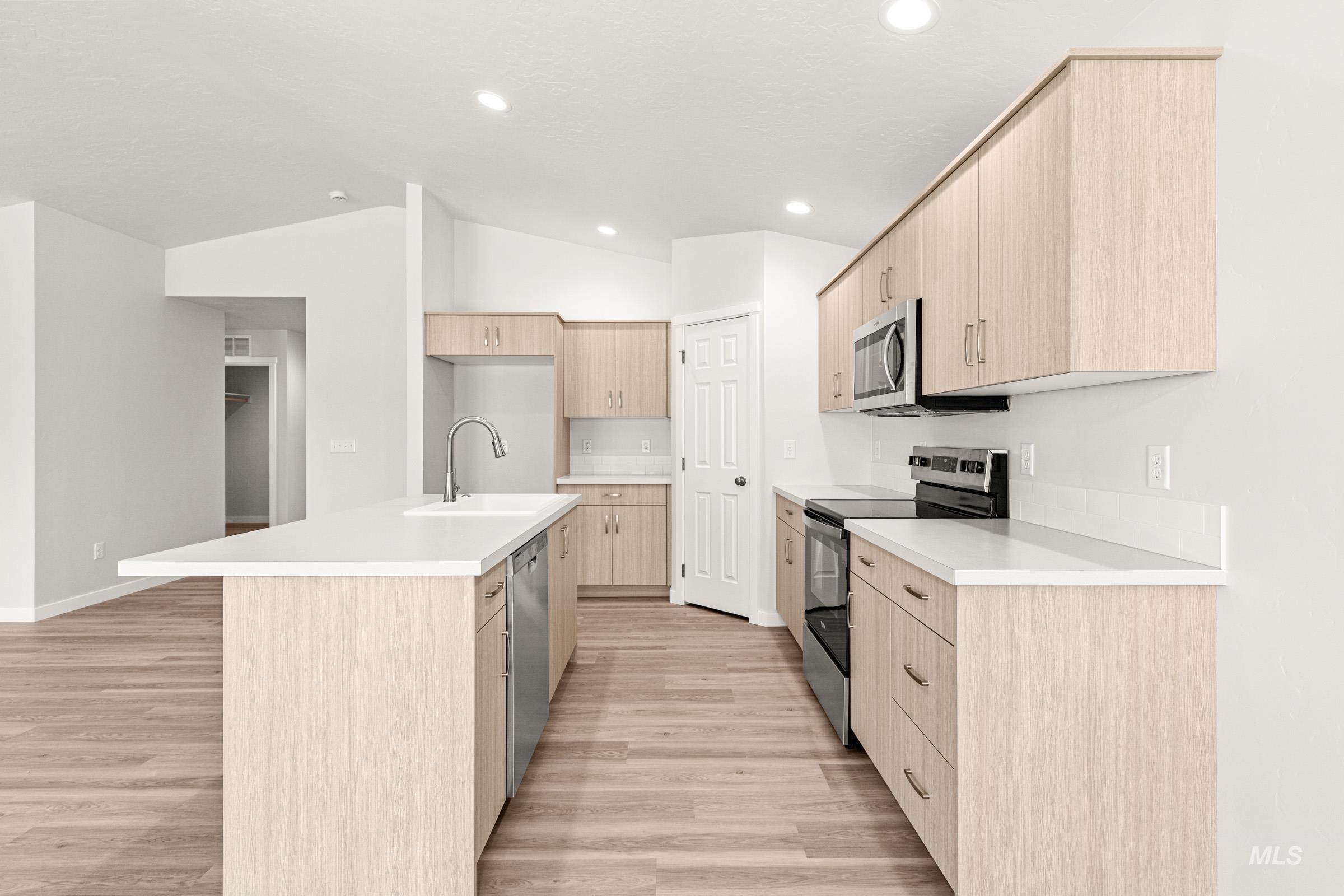 13736 Inman Court Caldwell, ID 83607 - Photo 6 of 20 Kitchen featuring light wood finish cabinetry, a center island with sink, stainless steel appliances, and lofted ceiling