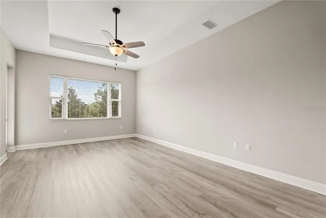 an empty room with wooden floor a ceiling fan and windows