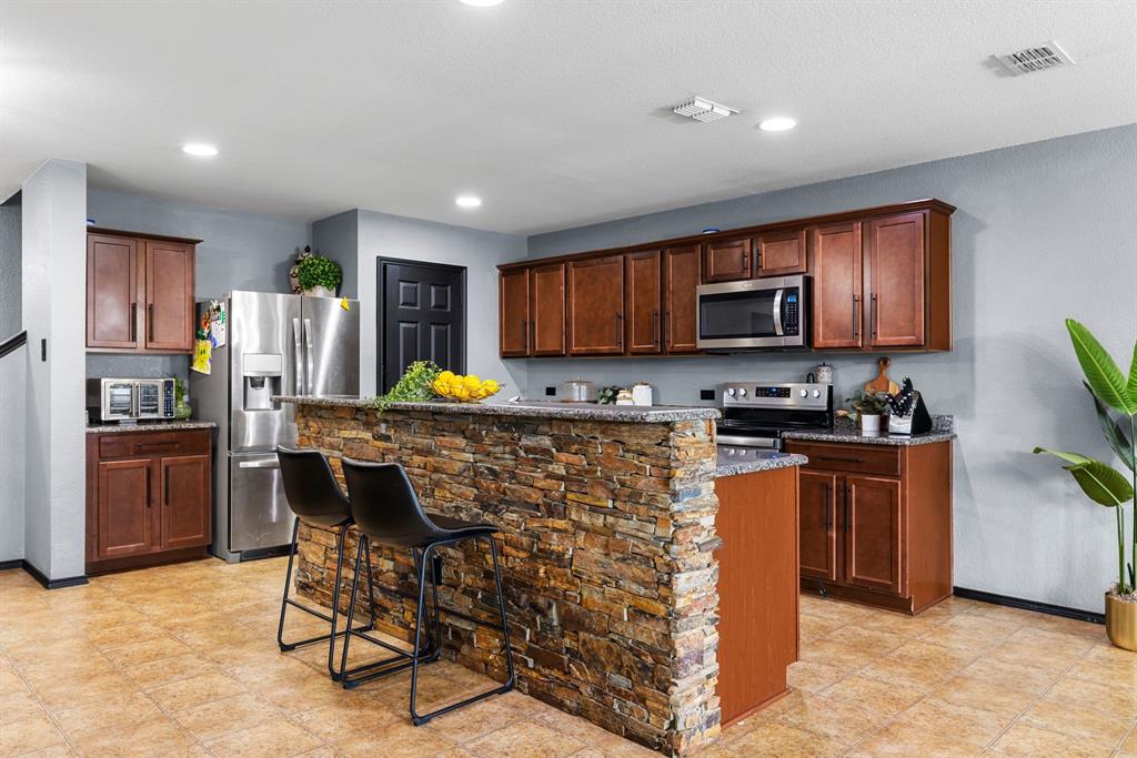 1014 Rio Frio Drive Forney, TX 75126 - Photo 13 of 19 Kitchen with a kitchen breakfast bar, appliances with stainless steel finishes, dark stone countertops, recessed lighting, and a center island