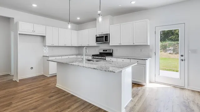 a kitchen with stainless steel appliances granite countertop a stove a sink dishwasher and a refrigerator with white cabinets