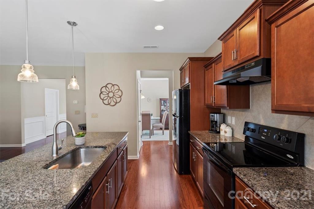 8098 Bryson Road Indian Land, SC 29707 - Photo 12 of 30 a kitchen with granite countertop stainless steel appliances a sink a stove top oven a chimney cabinets and wooden floor