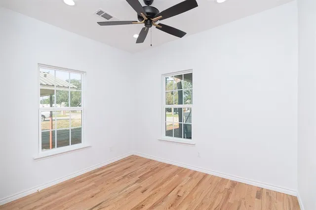 an empty room with wooden floor fan and windows