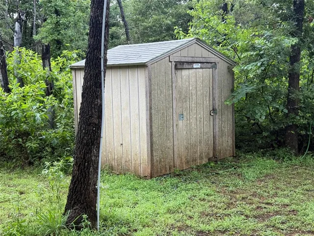 a view of a wooden house with a small yard and large trees