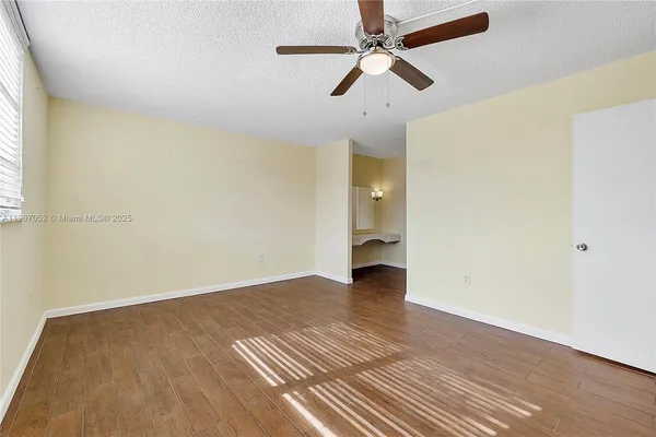 an empty room with wooden floor ceiling fan and windows
