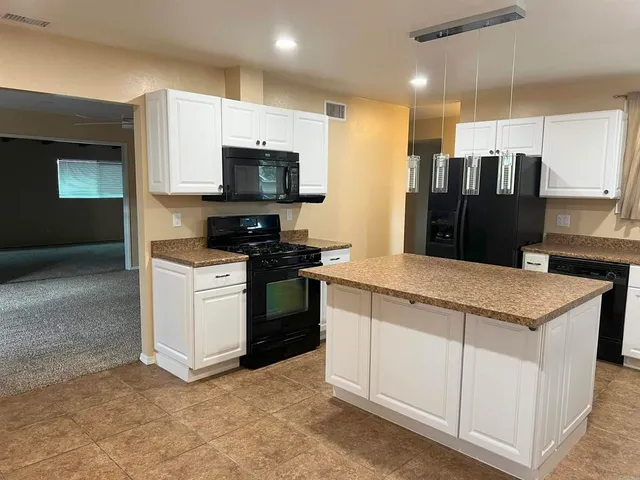 a kitchen with stainless steel appliances kitchen island granite countertop a refrigerator oven a sink dishwasher and white cabinets with wooden floor