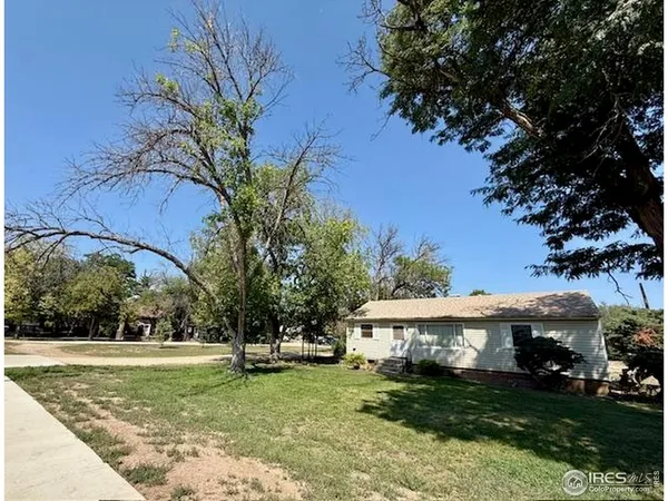 a view of a white house with a big yard and potted plants and large trees