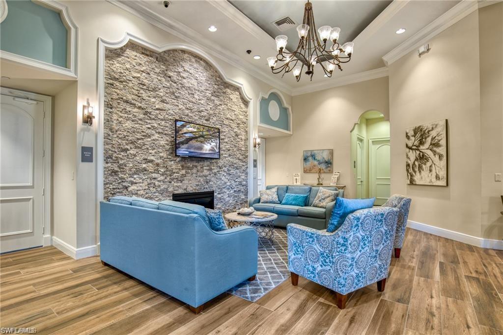1415 Princess Sabal Point Naples, FL 34119 - Photo 38 of 42 Wood-finish flooring, stone accent wall, crown molding, built-in fireplace, and a decorative chandelier