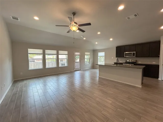 a view of an empty room and kitchen with wooden floor and fan