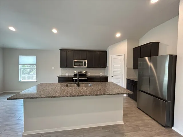 a kitchen with granite countertop a refrigerator and a stove top oven