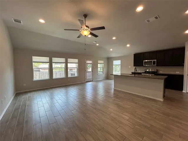 a view of an empty room with kitchen and window
